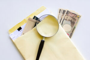 お金と書類と虫眼鏡の画像
